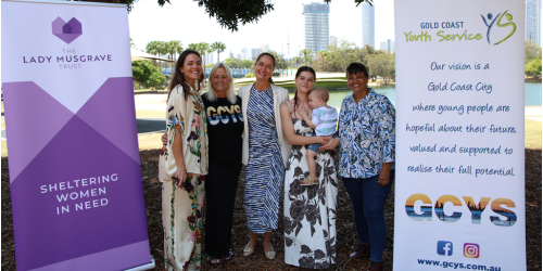 Four women, one holding a baby posing for a photo between the LMT and GCYS banners